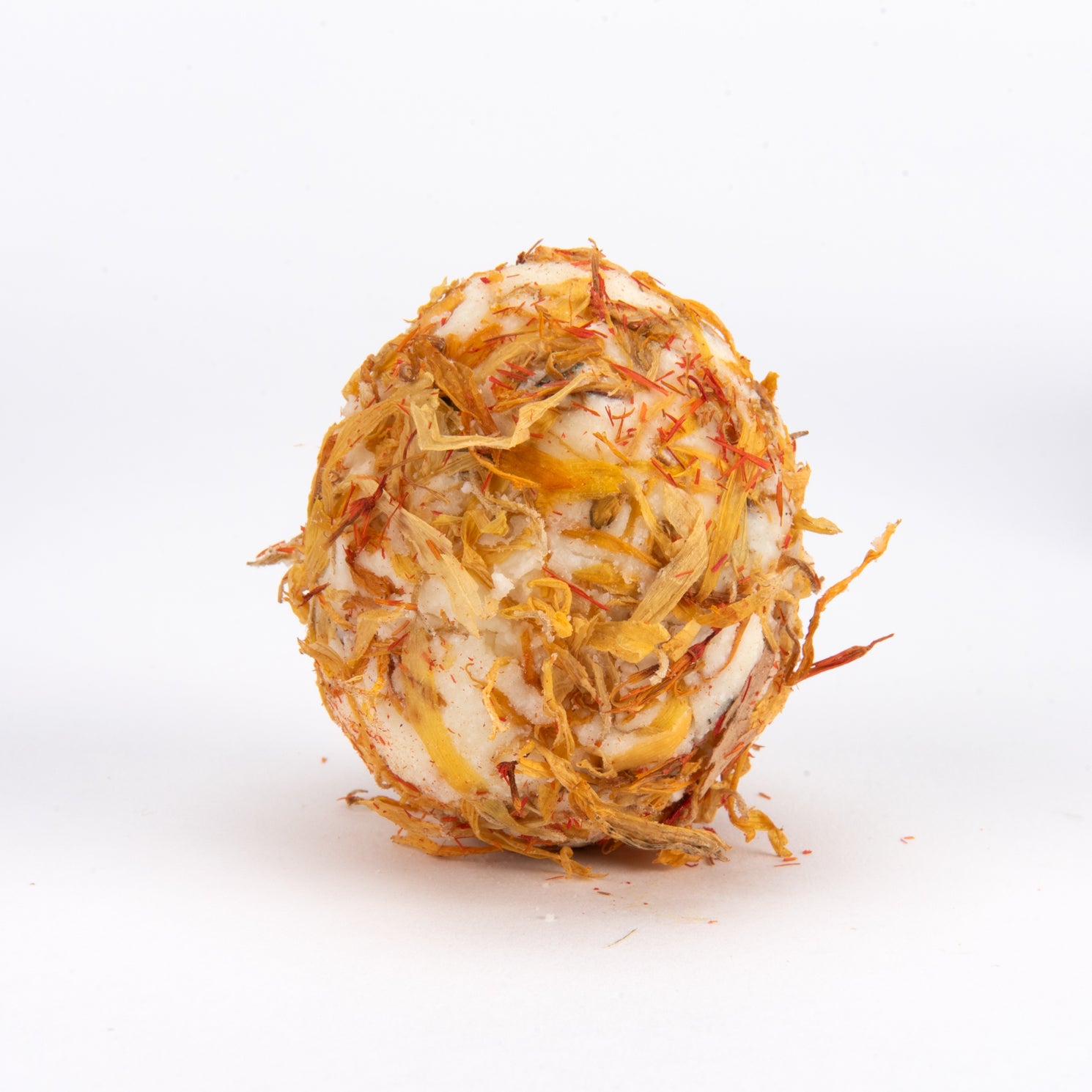 A spherical bath bomb made from dried orange calendula flowers and white soap, standing upright on a white background.