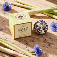 A square box of Heyland Whittle Wild Lemongrass Bath Melt sits on a rustic wooden surface, styled with dried cornflowers, fresh cornflower stems, and a wrapped bath ball.