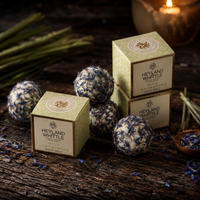 Three square boxes of Heyland Whittle Lemon Breeze Bath Milk are arranged on a rustic wooden surface with several blue-and-white marbled bath balls and dried botanicals around them.
