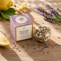 Heyland Whittle London Citrus & Lavender Bath Melts shown as a purple patterned box next to a dried lavender and citrus bath bomb, styled on a wooden table with lemon slices and lavender sprigs.