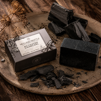 A boxed bar of charcoal soap and loose charcoal pieces arranged on a round stone tray over a rustic wooden surface. The box reads 'HEYLAND WHITTE ACTIVATED CHARCOAL'.
