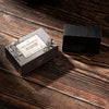 A dark charcoal-colored bar of soap sits next to its gray packaging box on a rustic dark wood background. The box features a white label with the brand name 'Heyland & Whittle' and the scent 'Active Charcoal'.
