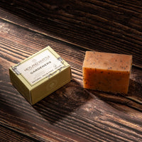 A rectangular bar of Heyland Whittle Gardeners natural palm rice soap next to its gold-colored branded box, displayed on a dark rustic wooden surface.