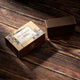 A rectangular bar of dark brown soap sits beside its decorative cardboard box on a rustic dark wood surface. 