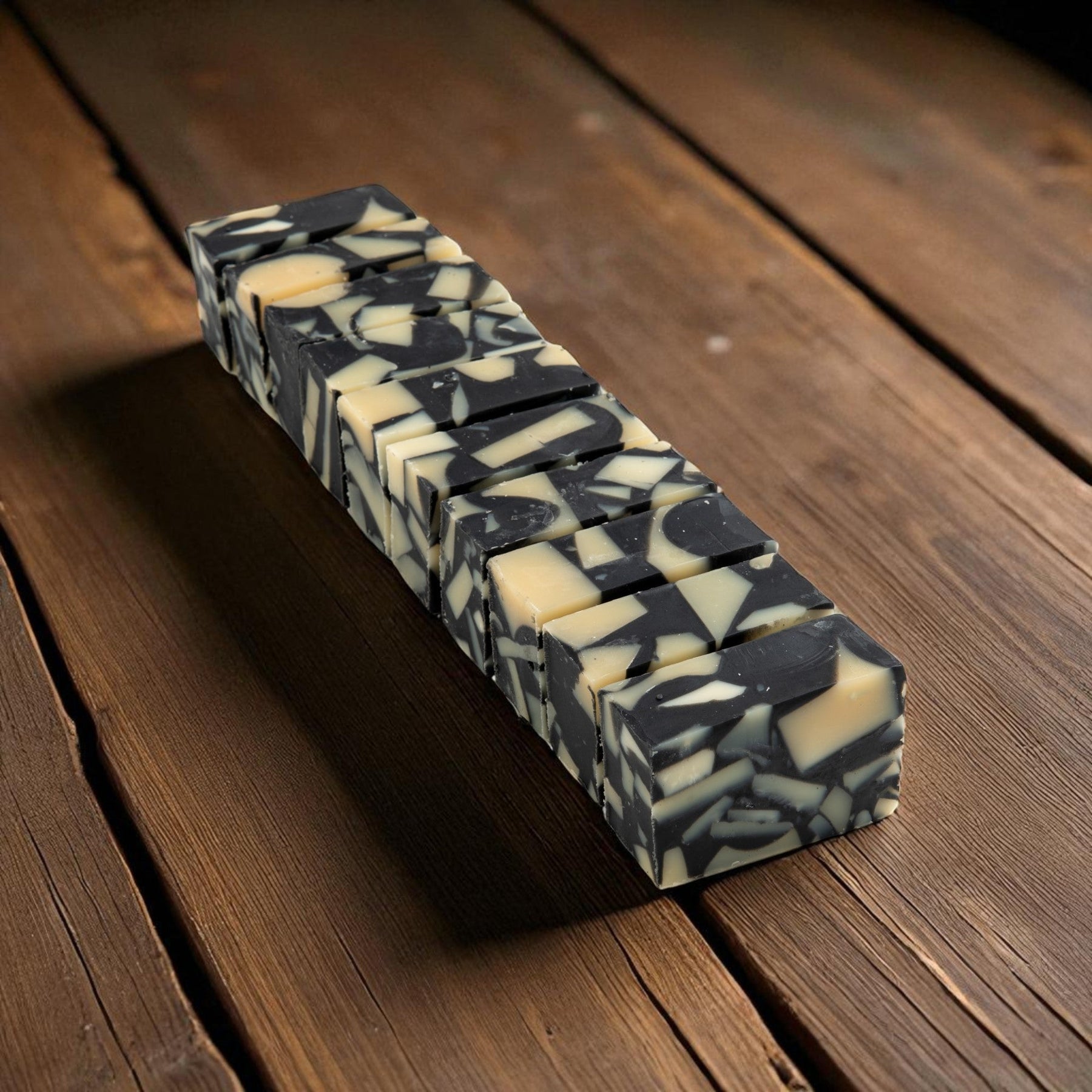A stack of rectangular bars of soap with a marbled black and cream pattern, arranged diagonally on a dark brown wooden surface.