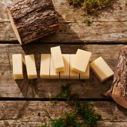 Several pale cream bars of soap arranged on rustic wooden planks, with pieces of bark and small green moss around them.