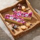 Two gold gift boxes filled with pink tissue paper and assorted gourmet chocolates, arranged on a rustic wooden serving tray with cheese slices and marbled stone surface.