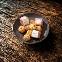 A dark ceramic plate holding several bath melts, with two small pink-and-white branded boxes placed on top, set on a rustic dark wooden surface.