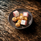 A dark ceramic plate holding several bath melts, with two small pink-and-white branded boxes placed on top, set on a rustic dark wooden surface.